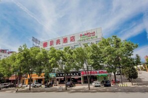A hotel with a large sign, trees in front, and several cars parked. - Shell Hotel (Chaoyang shoe city store, Chaoyang Street, Taiyuan) (Taiyuan)