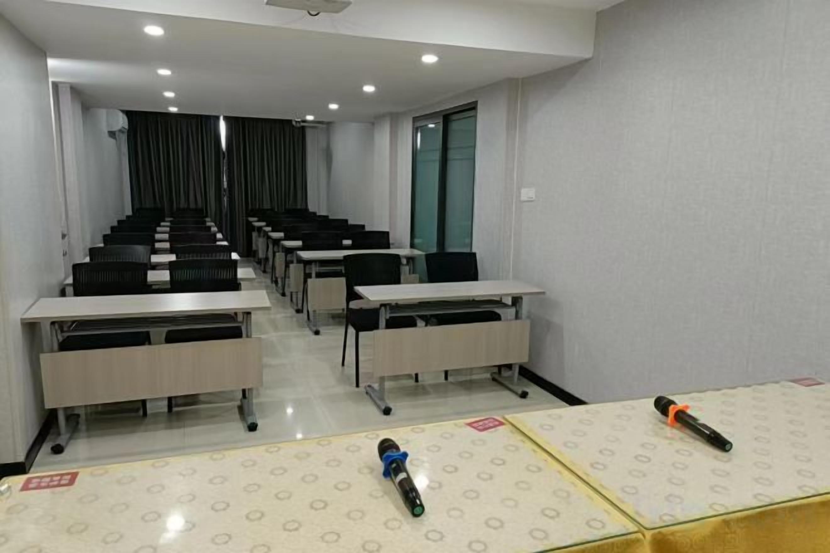 Una sala de conferències amb files de taules i cadires, un projector i un terra amb moqueta.