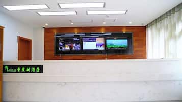 Een receptiebalie van een hotel met een flatscreen televisie waarop diverse content wordt getoond, een houten paneelwand en een naambord.