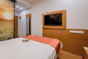Una habitación de hotel con una cama, un televisor instalado en la pared y una puerta que da a otra habitación.