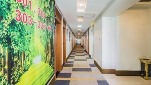 Ein Hotelkorridor mit Schachbrettfußboden, grüner Wand mit Nummern und Türen an beiden Seiten.