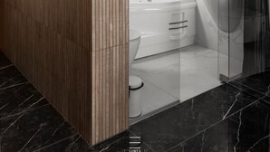 Un baño moderno con pared de paneles de madera, cabina de ducha de vidrio, bañera blanca y suelo de mármol.