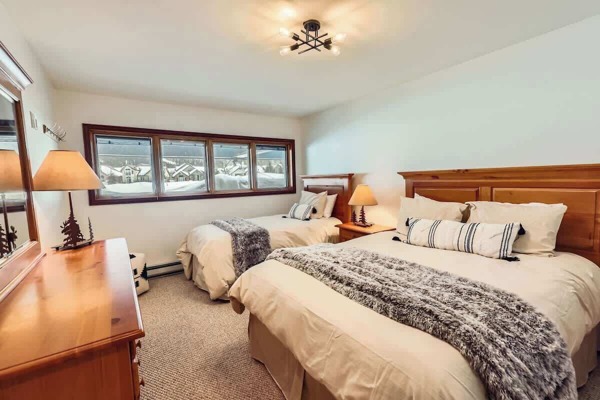 Une chambre avec deux lits, une commode en bois, une fenêtre donnant sur un paysage agréable et un luminaire au plafond.