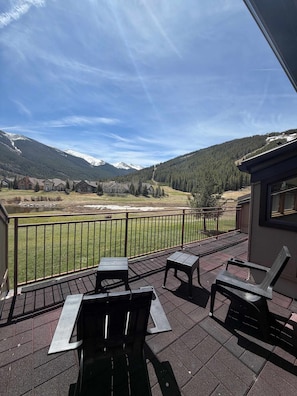 A balcony with outdoor seating, a view of a mountainous landscape, and a clear sky.