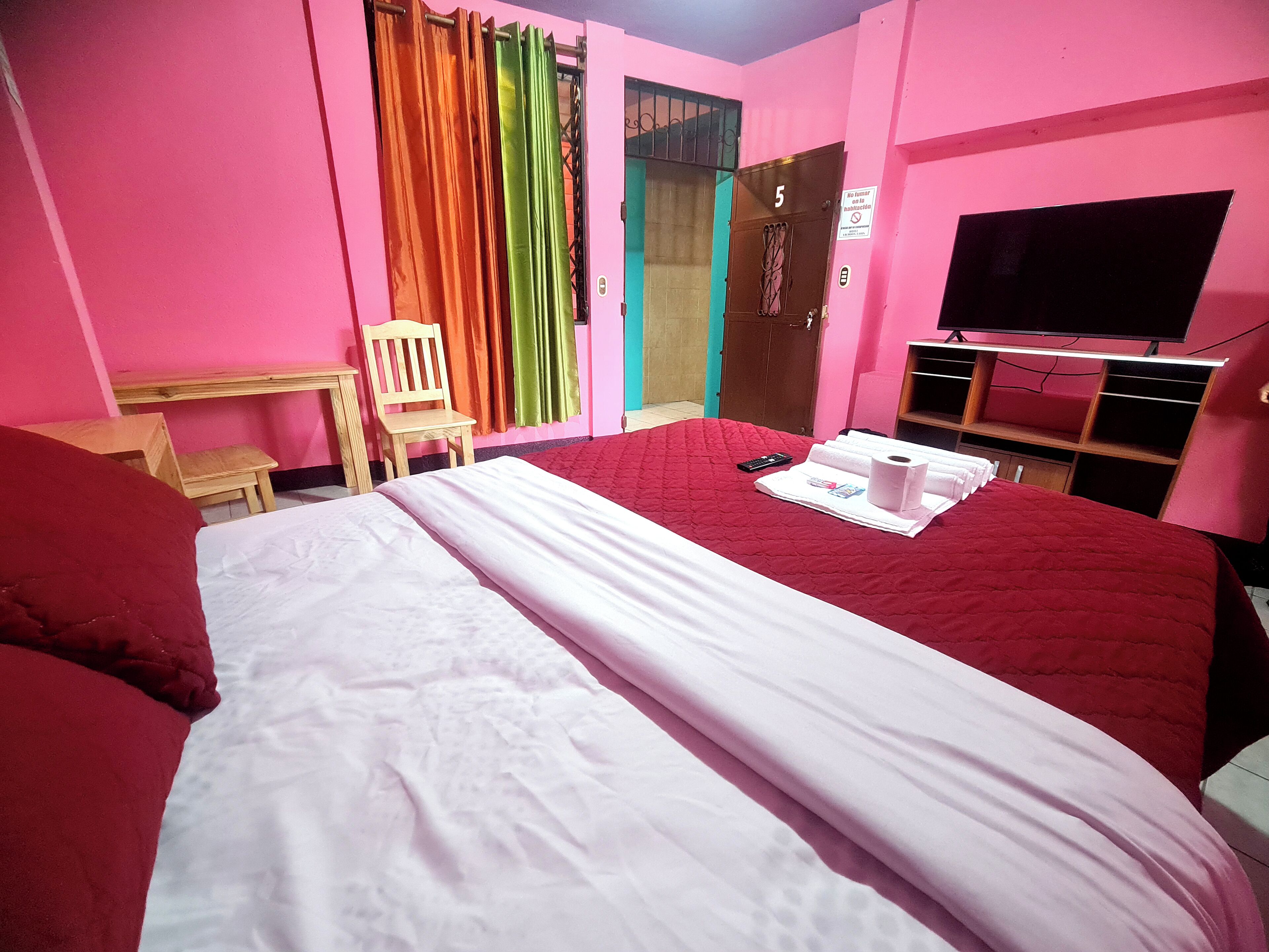 A hotel room with a bed, a chair, a TV, and a door with a number.