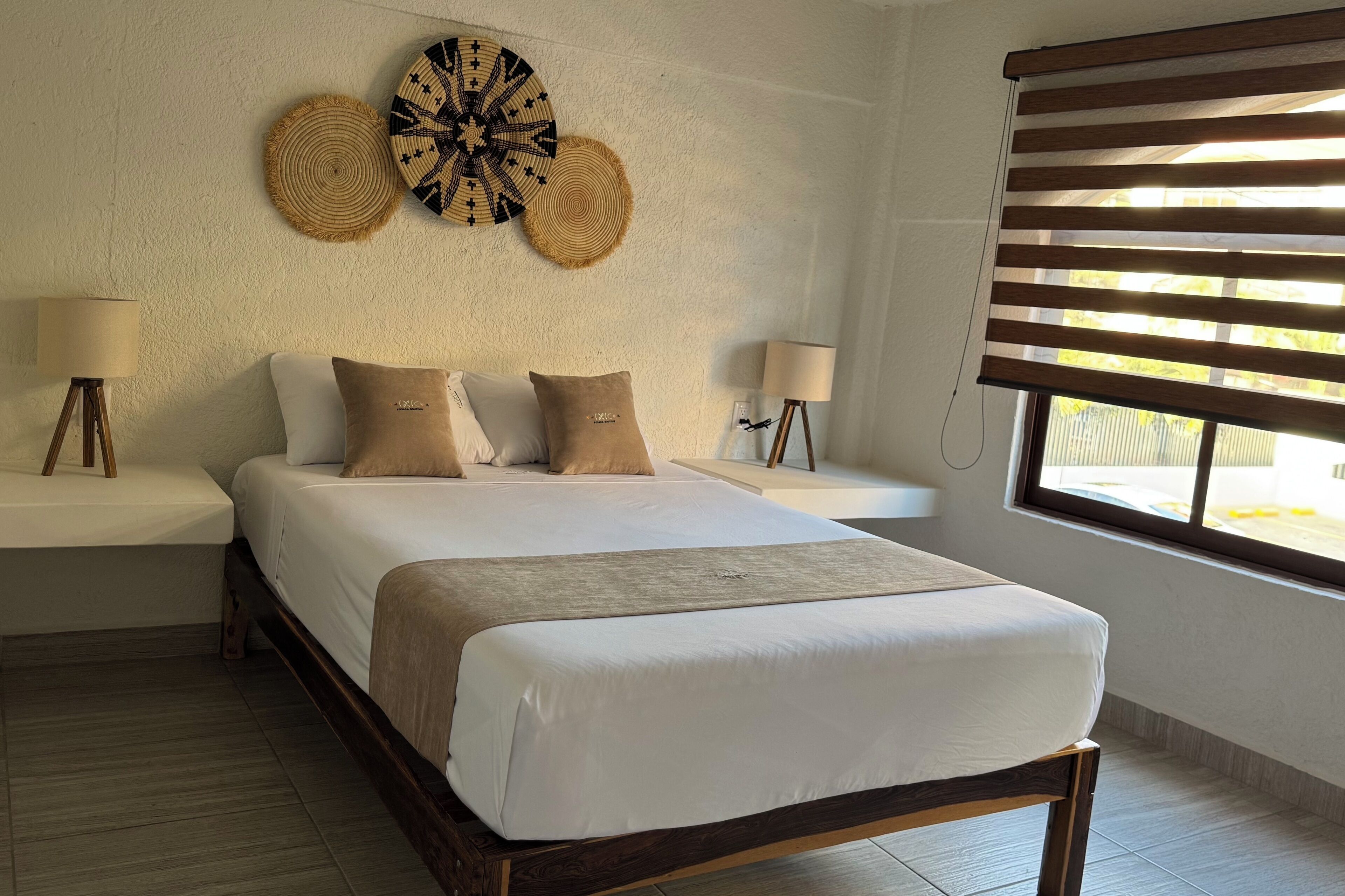 A bedroom with a bed, two bedside tables, wall decor, and a window with blinds.