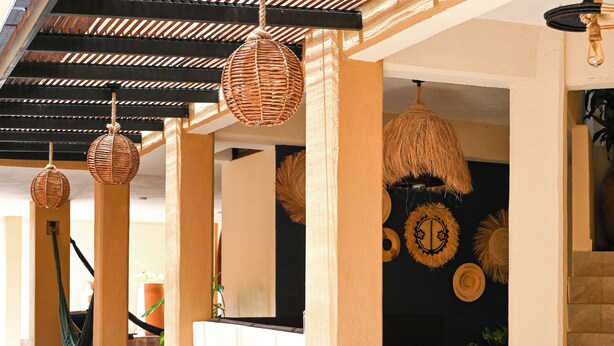 A hotel lobby with wicker hanging lamps, a reception desk, and a staircase.