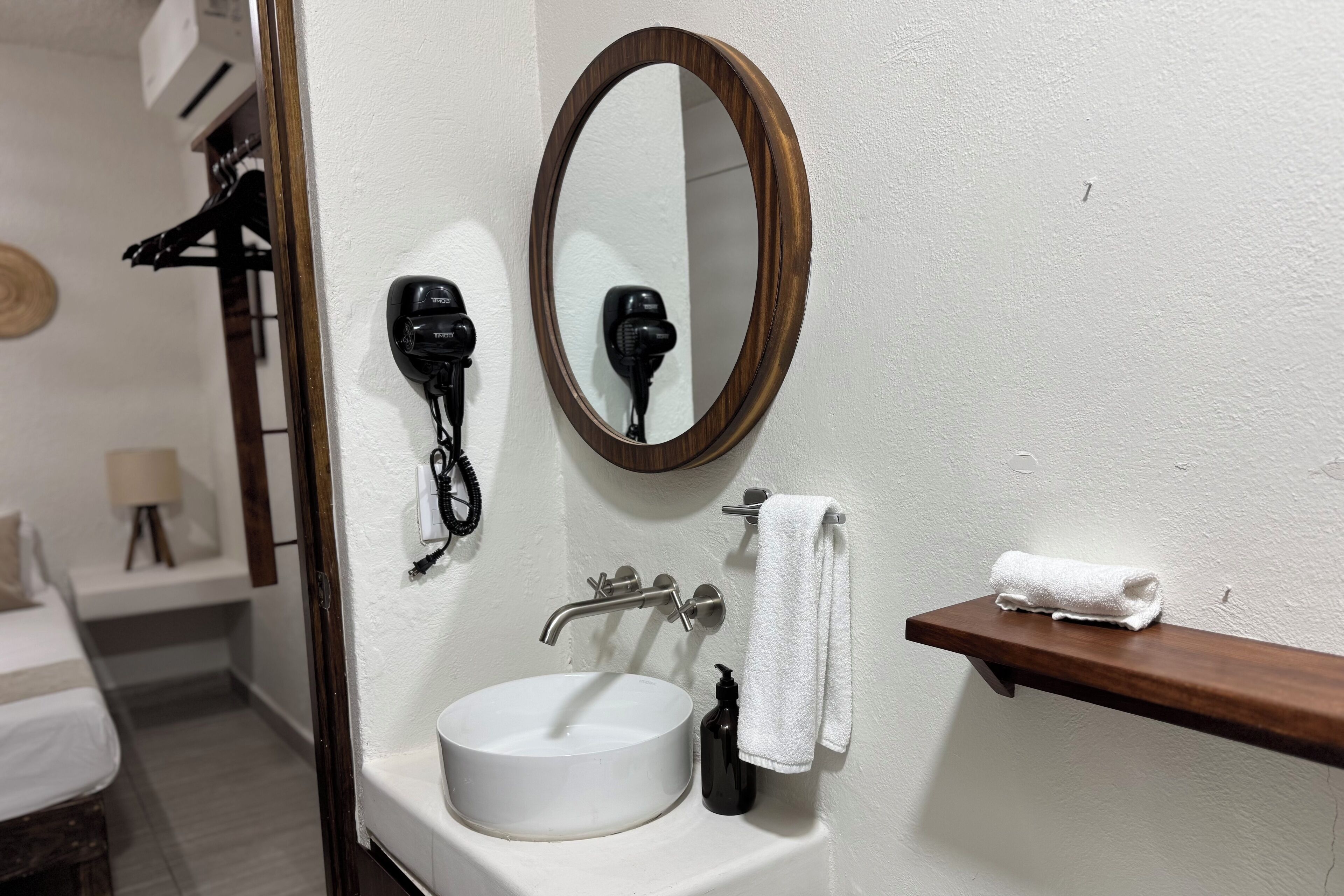 Un baño con un lavabo blanco, un espejo redondo, un perchero y un secador de pelo en la pared.