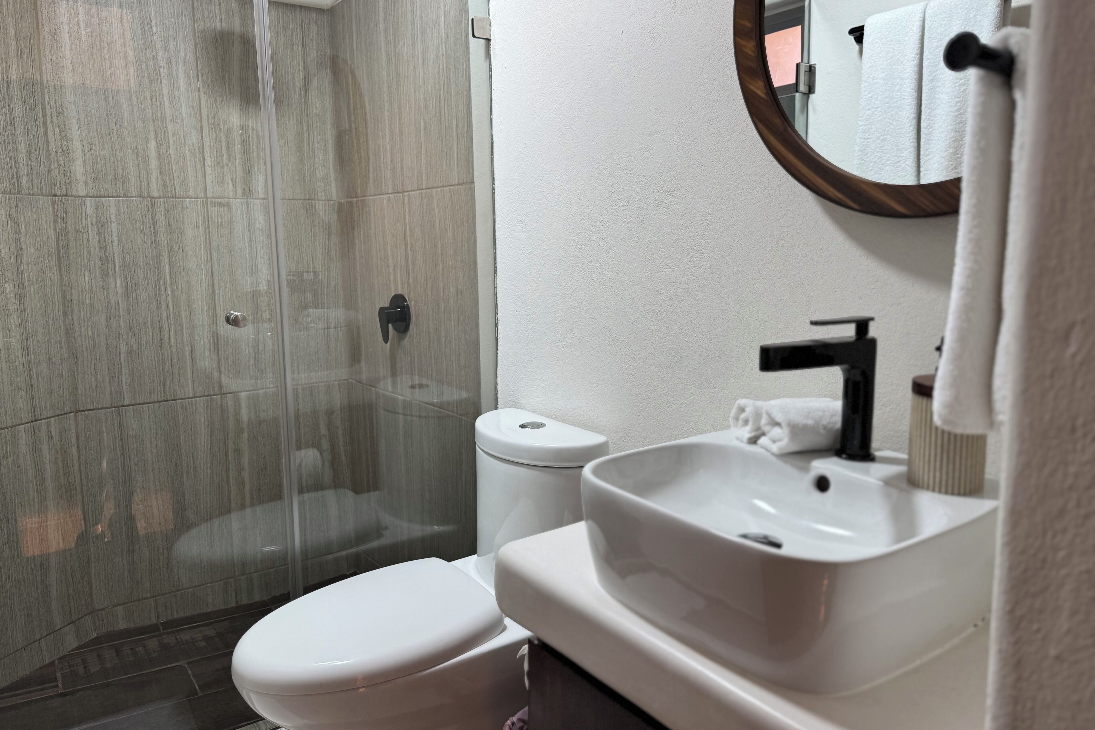 A bathroom with a glass-enclosed shower, a white toilet, and a white sink with a mirror above it.