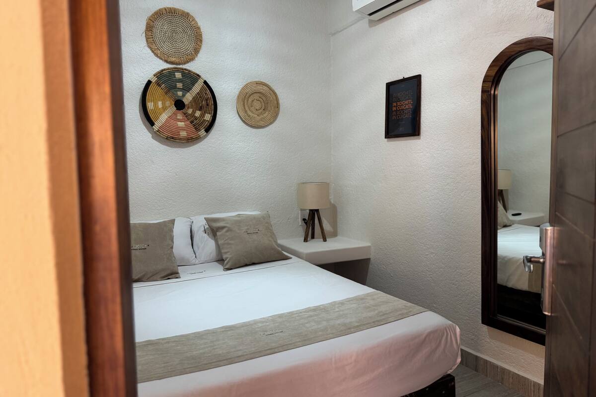 A hotel room with a bed, bedside table, lamp, wall decor, and a mirror.
