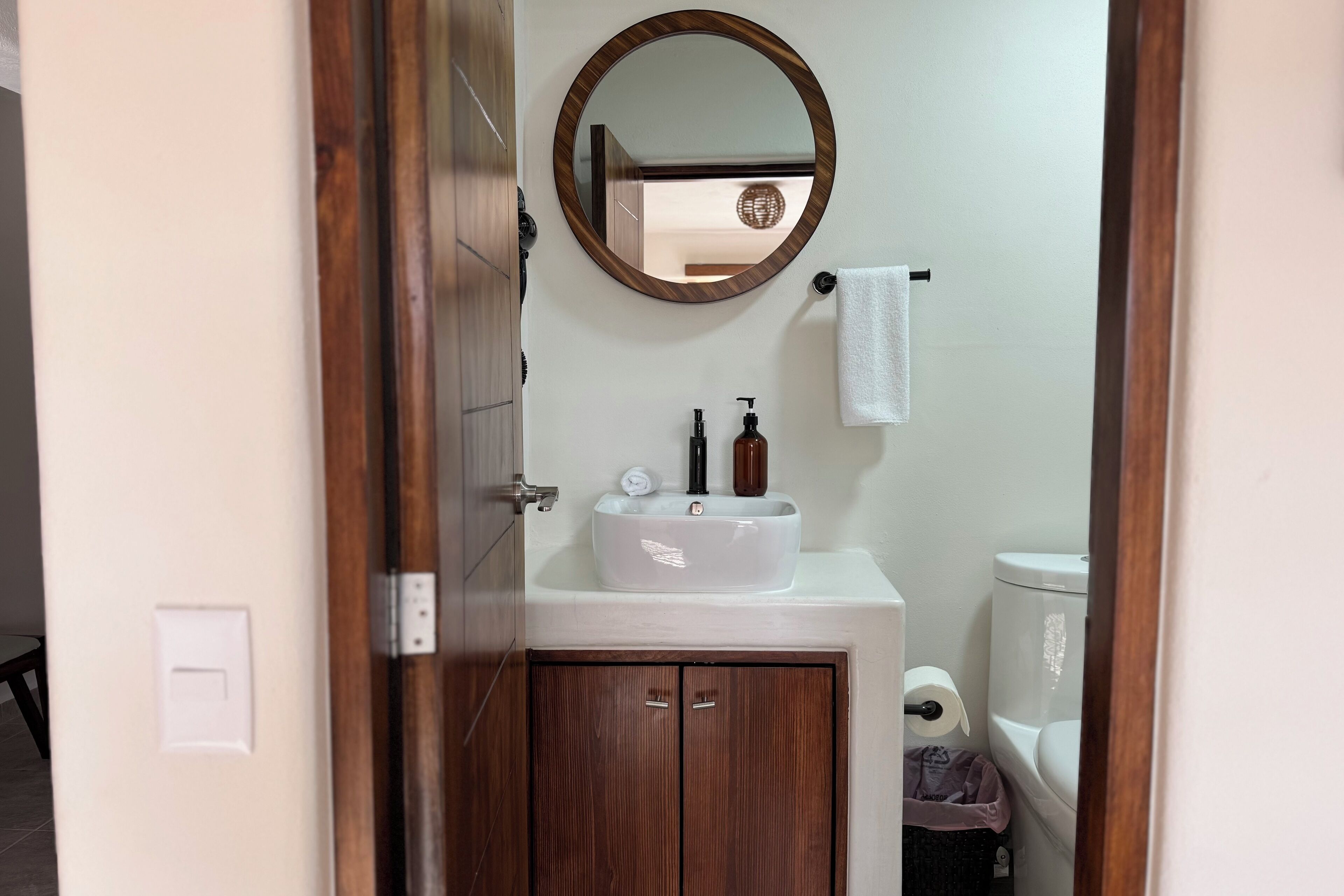 A bathroom with a wooden cabinet, a white sink, a mirror, and a toilet.