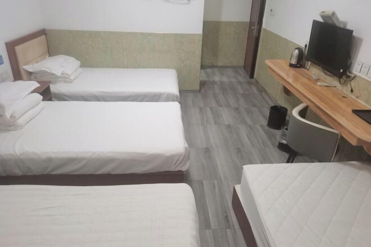 Ein Hotelzimmer mit drei Einzelbetten, einem Holztisch mit Fernseher und einer kleinen Mülltonne.