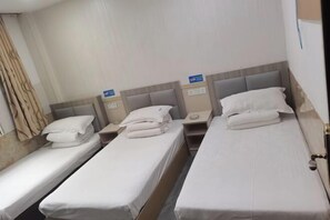 Ein Hotelzimmer mit drei Einzelbetten, jeweils mit Kissen und Nachttisch.
