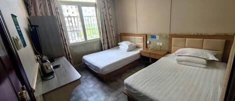 A hotel room with two single beds, a small desk with a kettle, a window with curtains, and a wall-mounted air conditioner.