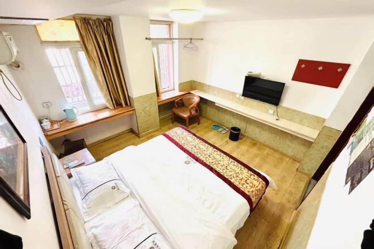 Une chambre d’hôtel avec un lit, un bureau et une chaise, une télévision et une fenêtre avec des rideaux.