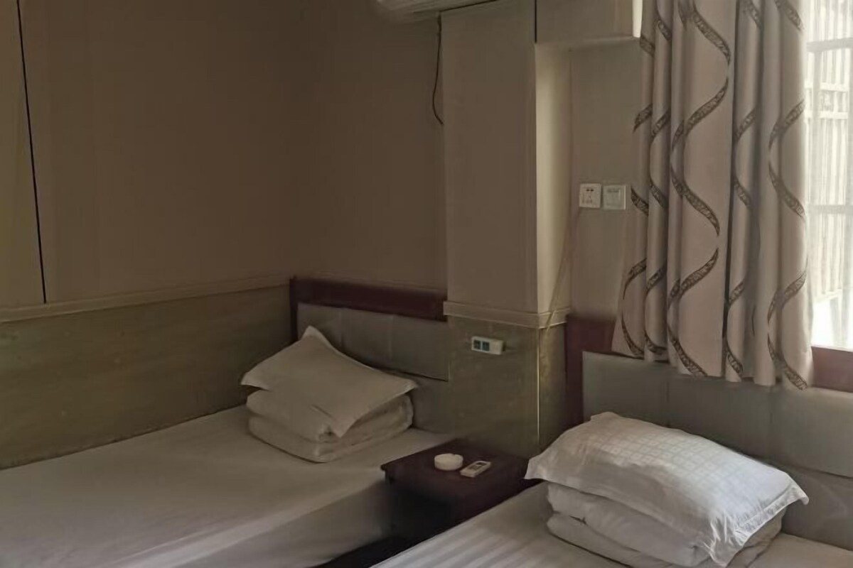 Ein Hotelzimmer mit zwei Betten, jeweils mit ordentlich gebetteter weißer Bettwäsche und Kissen. Es gibt einen kleinen Tisch mit einer Fernbedienung und einem dekorativen Gegenstand.