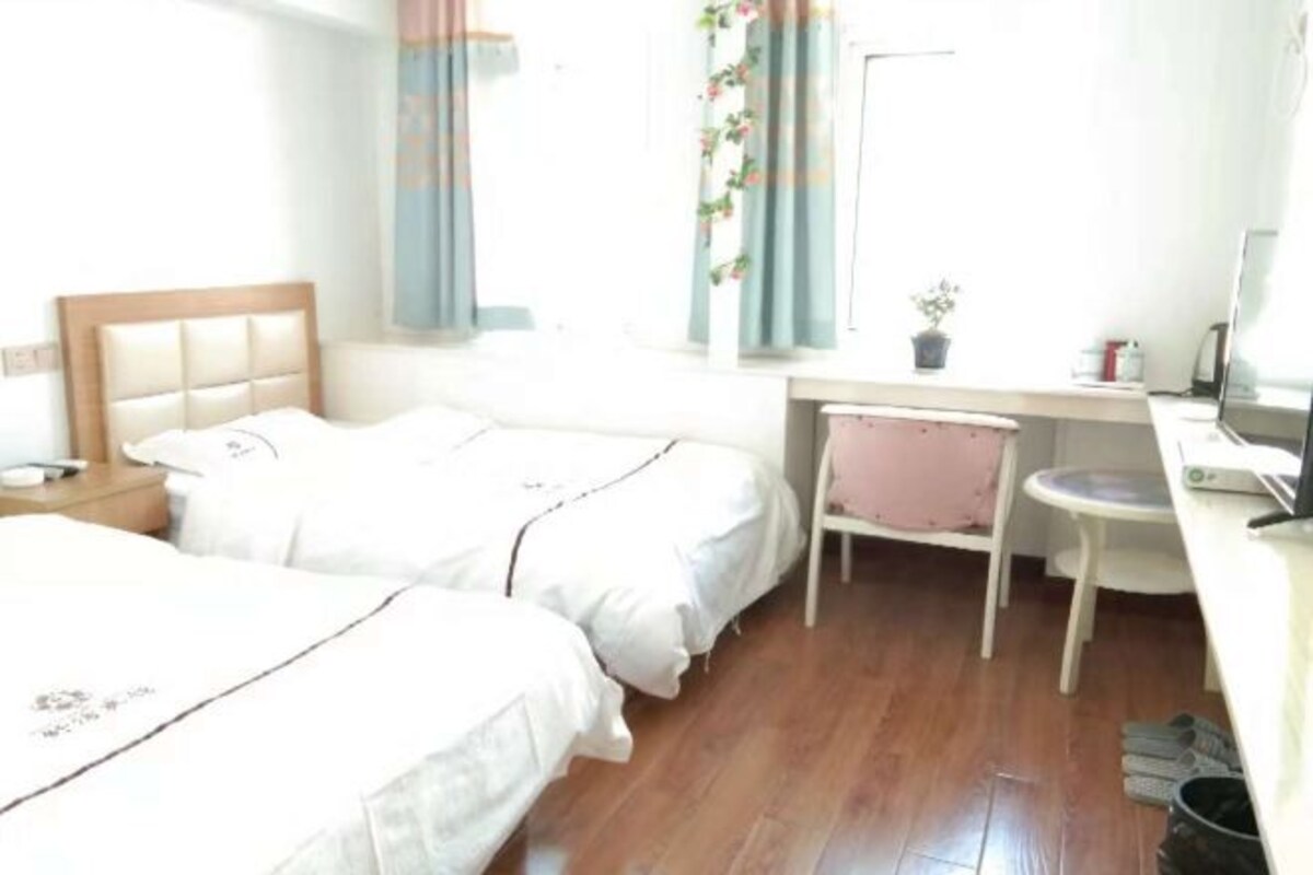 Een hotelkamer met twee bedden, een bureau, een stoel, een televisie en een raam met gordijnen.