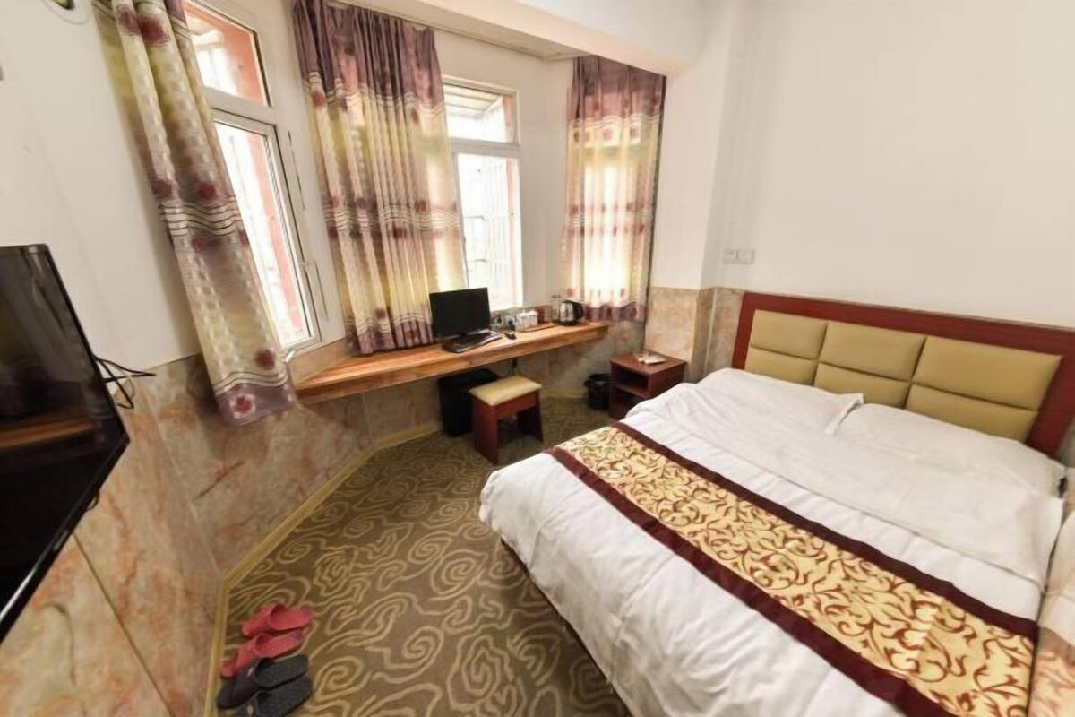 Une chambre d’hôtel avec un lit, un bureau avec un ordinateur, une télévision et une fenêtre avec des rideaux.