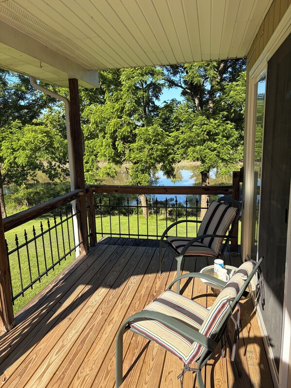 A wooden deck with two chairs and a table, overlooking a lake and trees.