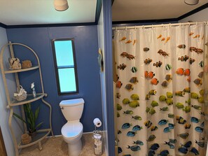 Bagno con un water, una finestra, uno scaffale con oggetti decorativi e una tenda da doccia con motivi di pesci.