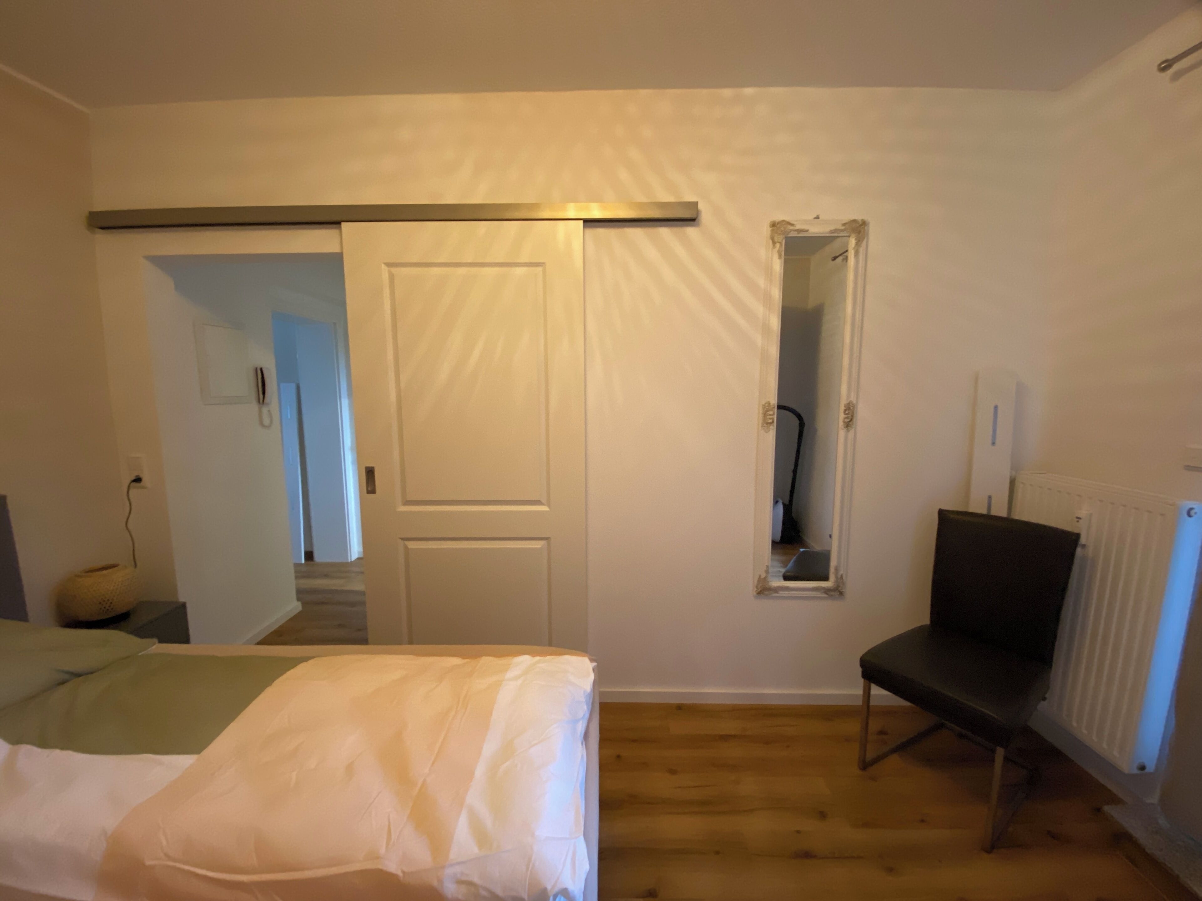 Un dormitorio con una cama, una silla, un televisor, un radiador y una puerta con espejo.