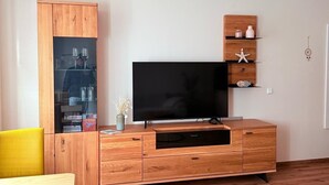 Una sala de estar con un mueble de televisión de madera, un aparador de vidrio y un sillón amarillo.