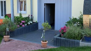 Un edificio de dos pisos con fachada amarilla, puerta gris y un balcón con macetas colgantes de flores.