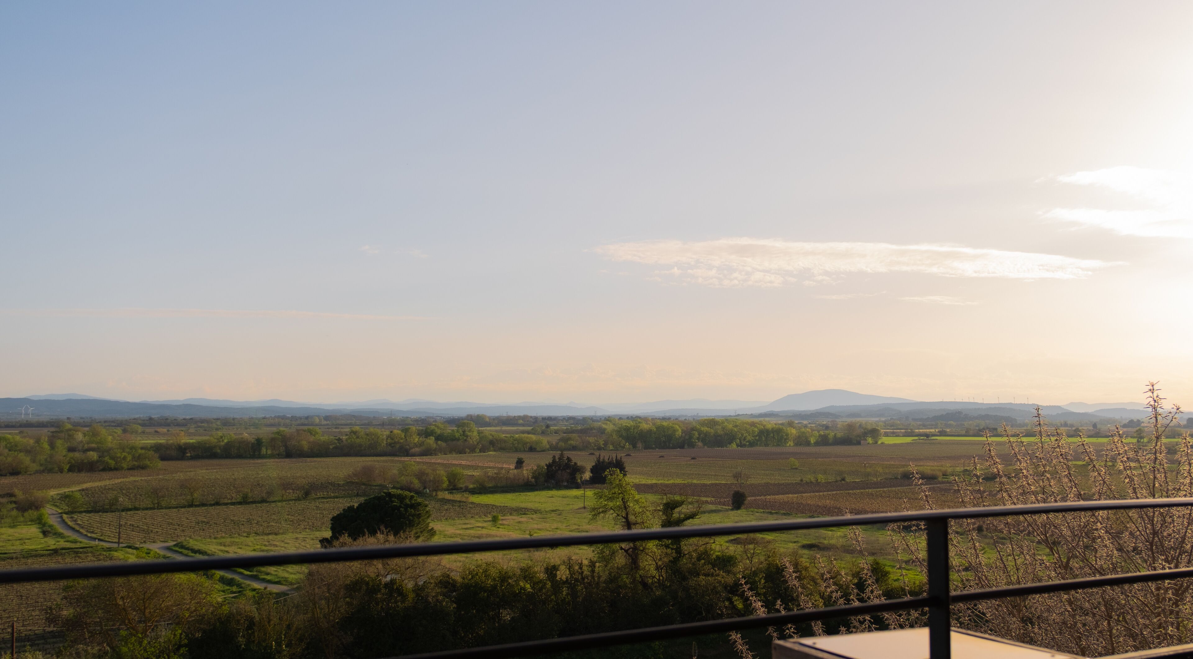 Une vue magnifique depuis un balcon donnant sur un paysage rural, avec des champs, des arbres et des montagnes à l’horizon.