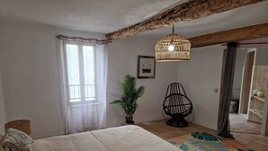 A bedroom with a large bed, a hanging light fixture, a potted plant, and a chair.