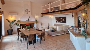 A spacious living area with a wooden dining table, comfortable seating, a sofa, and a kitchen area with a chimney.