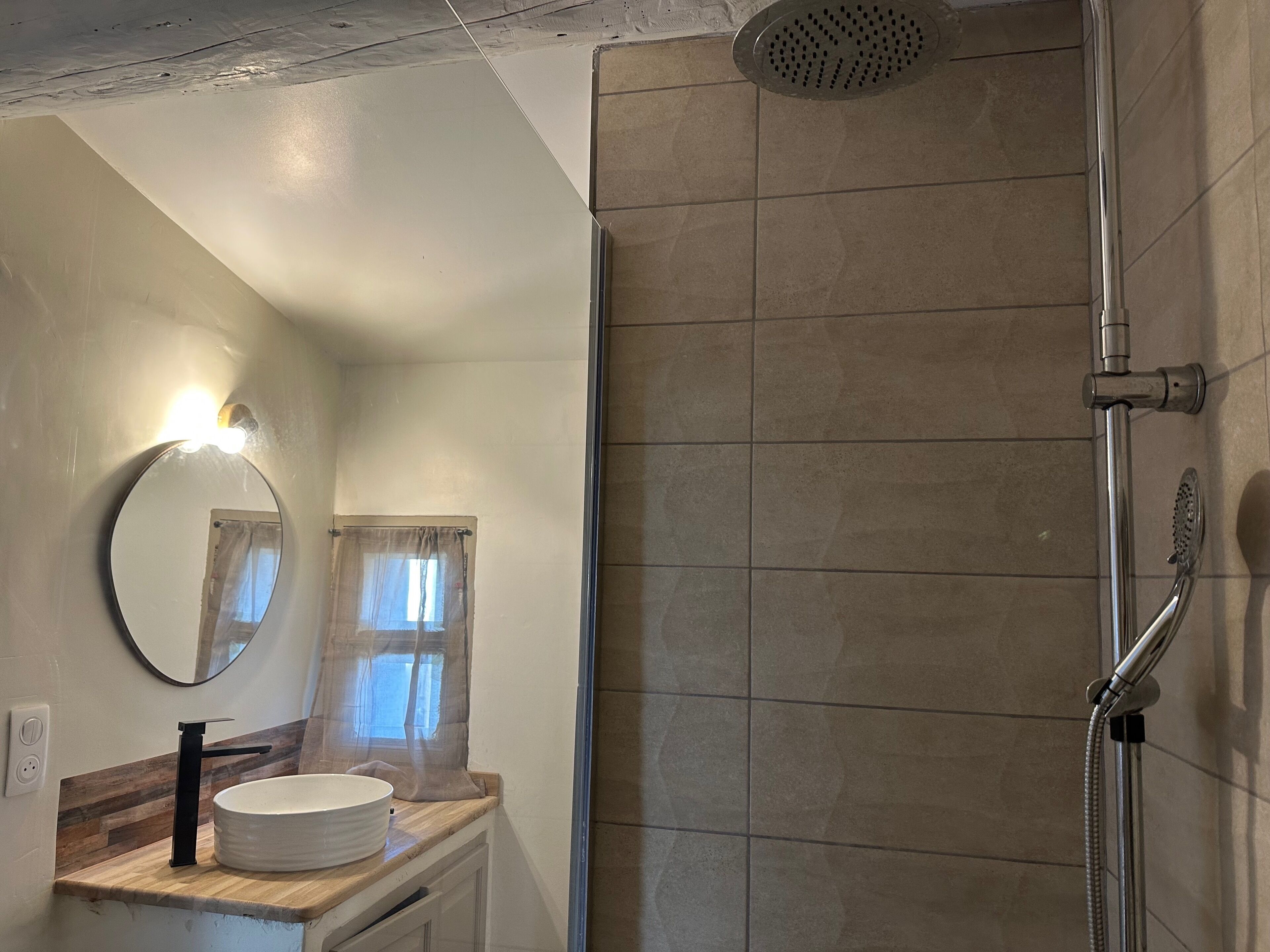 A bathroom with a shower, a sink with a mirror, and a window with curtains.