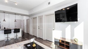 A modern living room with a TV, bar stools, and a coffee table. - Lux Noir ATL High-rise self check-in Balcony views (Atlanta)