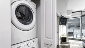 A modern laundry room with stacked washers and dryers, a door leading to a balcony with outdoor seating. - Lux Noir ATL High-rise self check-in Balcony views (Atlanta)