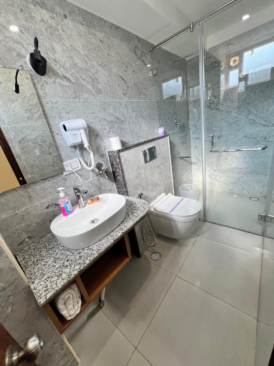 A modern bathroom with a marble sink, a glass shower enclosure, and a toilet.
