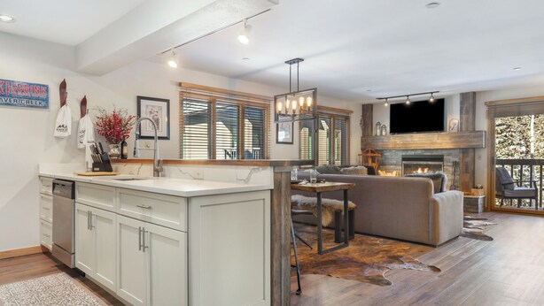 A modern kitchen with white cabinetry, a central island, and a dining area with a fireplace. - Mountain Modern Ski In-Ski Out Condo With Hot Tub In Beaver Creek - 1BR/2BA (Beaver Creek)
