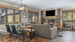 A modern living room with a fireplace, a dining area, and a large window with blinds. - Mountain Modern Ski In-Ski Out Condo With Hot Tub In Beaver Creek - 1BR/2BA (Beaver Creek)
