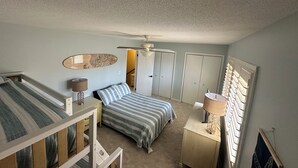 Une chambre avec un lit superposé, un lit simple, un ventilateur de plafond, une commode et un miroir au mur.