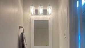 Un meuble-lavabo de salle de bain avec un lavabo en forme de bol de couleur bleue, un miroir au-dessus et trois appliques murales.