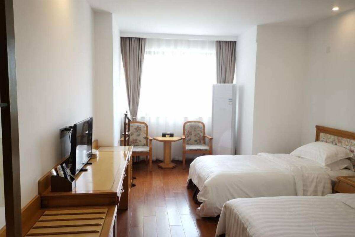 Een hotelkamer met twee bedden, een bureau, een televisie en een kleine tafel met stoelen.