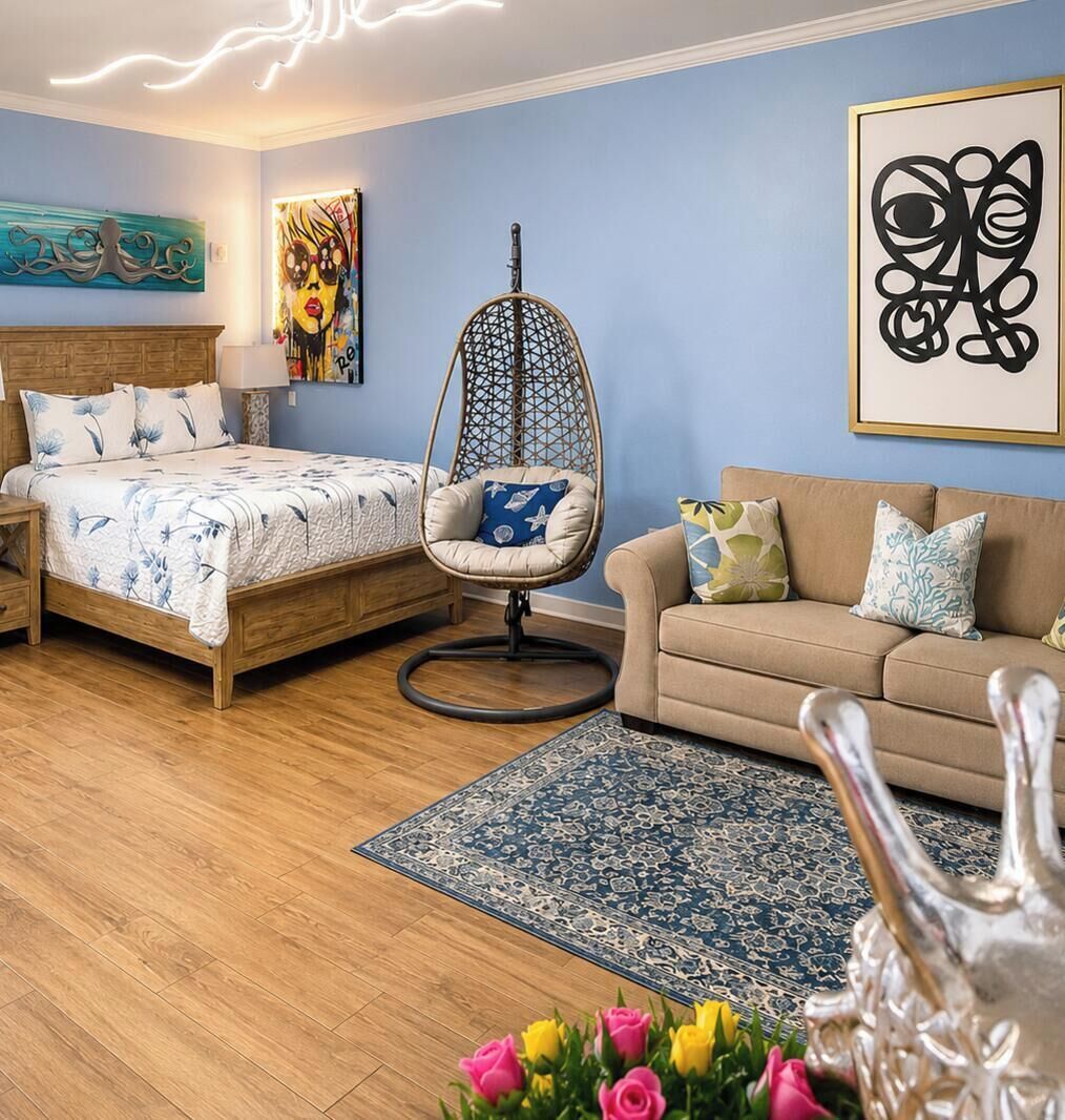 A bedroom with a bed, a hanging chair, a sofa, a rug, and a vase with flowers.