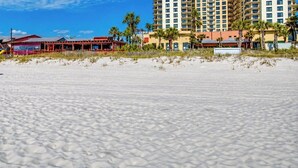 Ein Strand mit einer Struktur aus Schilfdach, ein Gebäude mit rotem Dach und ein Hochhaus-Hotel.