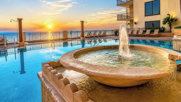 Ein Pool mit einer Springbrunnen, Liegestühlen und Blick auf den Sonnenuntergang.