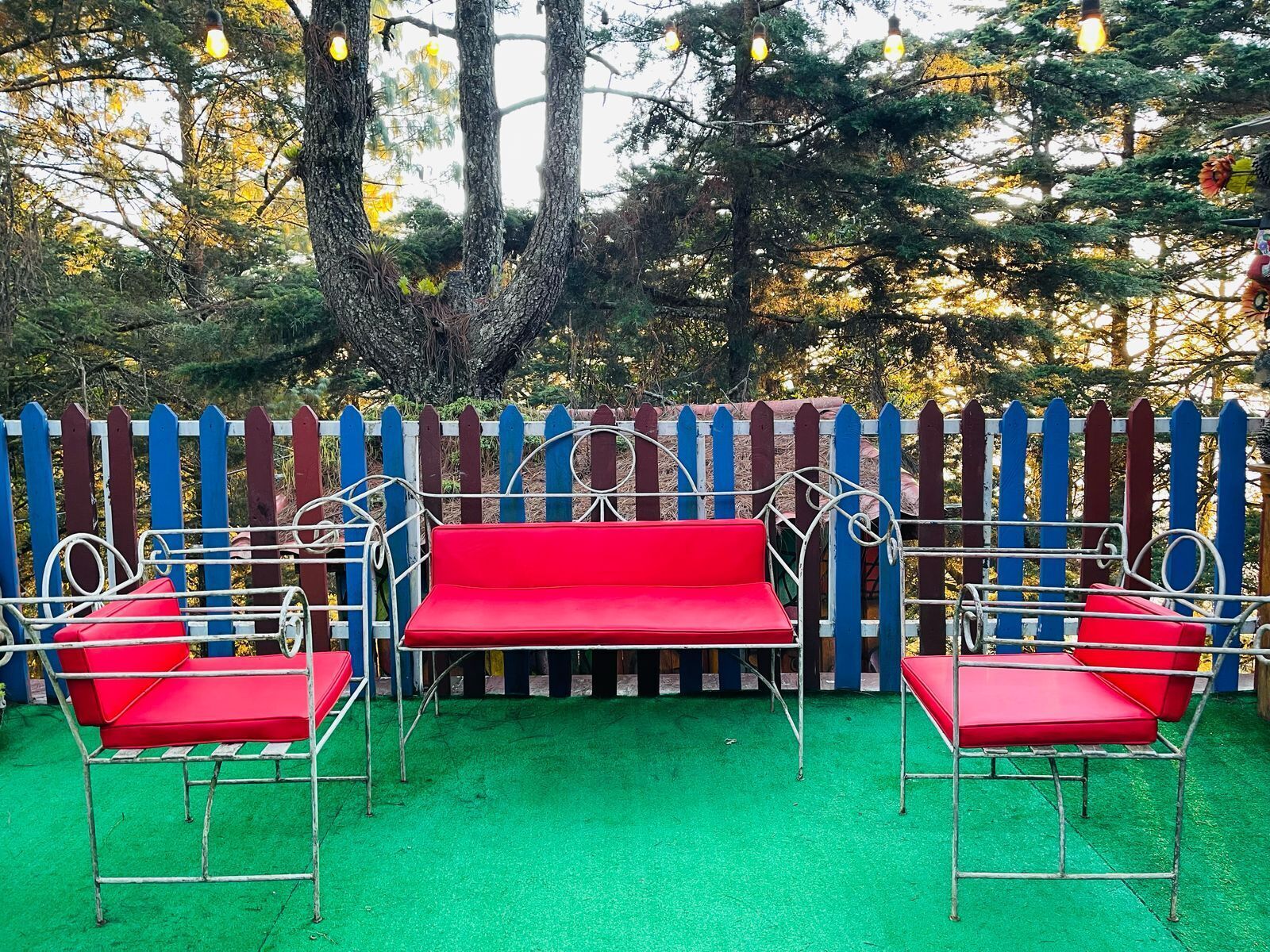 A red bench with metal frames, a white picket fence, and green artificial turf.
