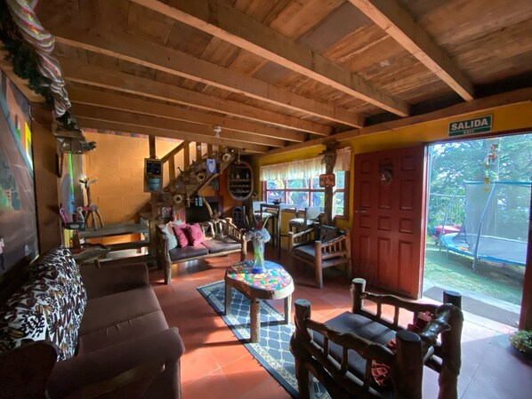 A cozy interior with a wooden ceiling, a sofa, a coffee table, and a red door labeled "SALIDA". - Hotel y Cabañas La Posada del Cielo (La Palma)