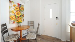 Un coin repas avec une table en bois, deux chaises, un vase de fleurs et un tableau représentant des tournesols accroché au mur.
