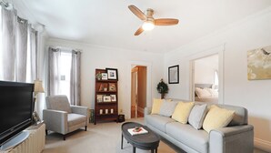 Un salon équipé d’un téléviseur, d’un fauteuil, d’un canapé, d’une table basse et d’un ventilateur de plafond.
