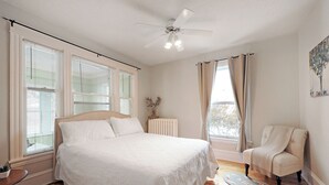 Une chambre à coucher avec un grand lit, une chaise, un radiateur et une fenêtre avec des rideaux.