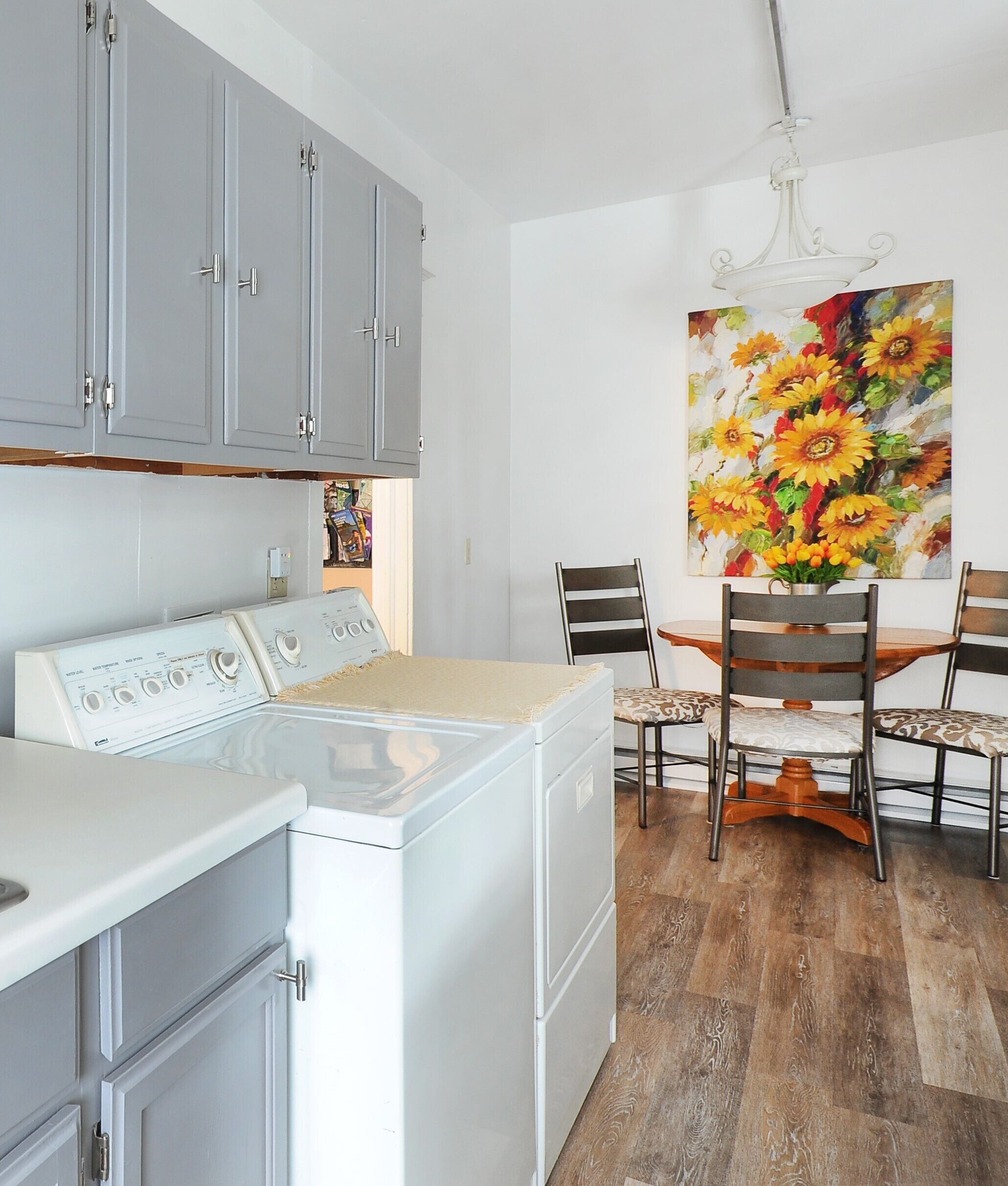 Una cocina con lavadora y secadora integradas, armarios grises y una zona de comedor con mesa y sillas.