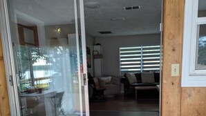 Una habitación con puerta de vidrio corredera que da a un balcón, piso de madera y un área de descanso con sofá y sillones.
