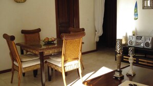 A dining area with a wooden table and chairs, a fruit bowl, and a radio on a shelf.